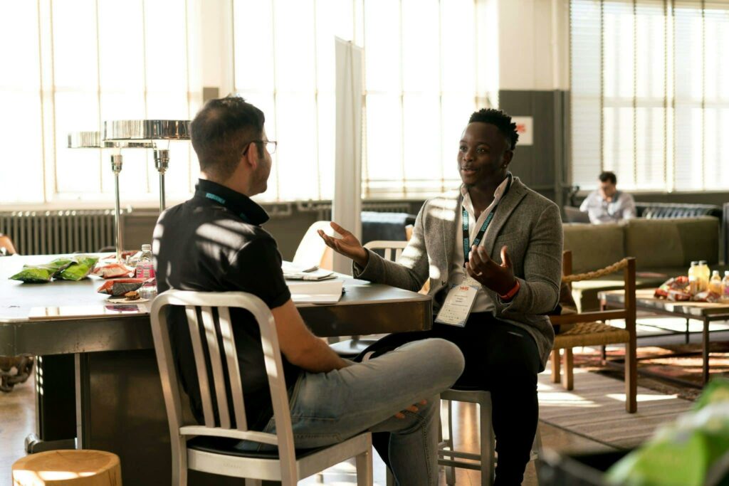 two men sit at a table to have a conversation while at a networking event, a great opportunity for real estate lead generation