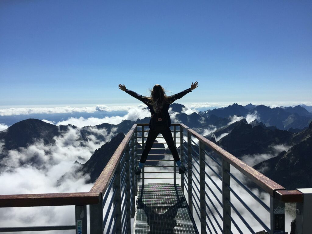 A woman stands at great heights overlooking mountains and clouds, representing successful real estate advertising