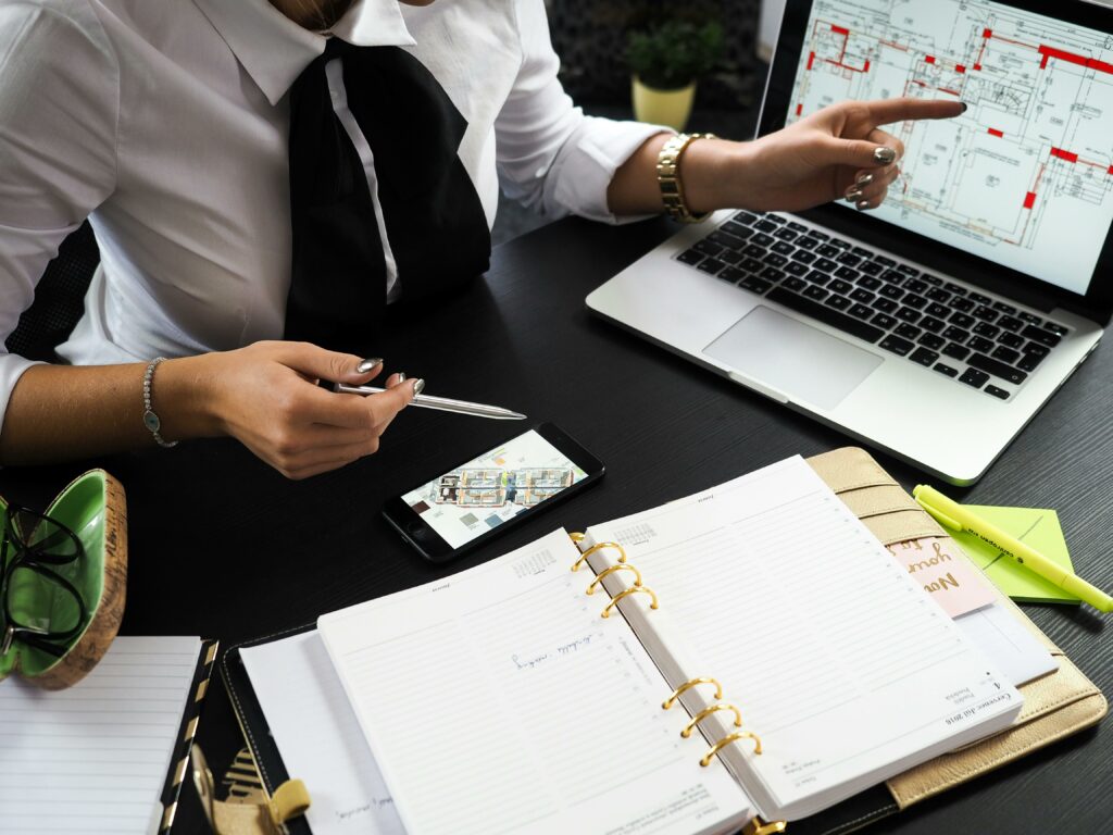 Professional woman at a desk looking at blueprints on a screen and additional papers, representing how top real estate agents are too busy and their time too valuable to do their own marketing.