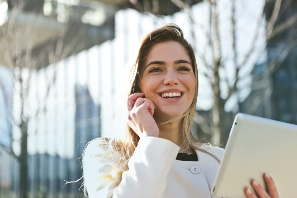 Woman in a blazer holds an ipad and smiles, representing freedom and success through successful real estate email campaigns and marketing by 23 Window Media.