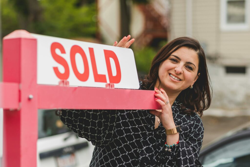 A woman real estate agent puts a ‘sold’ rider on a sign outside her listing after winning the new lead and seller client with door hangers for Realtors