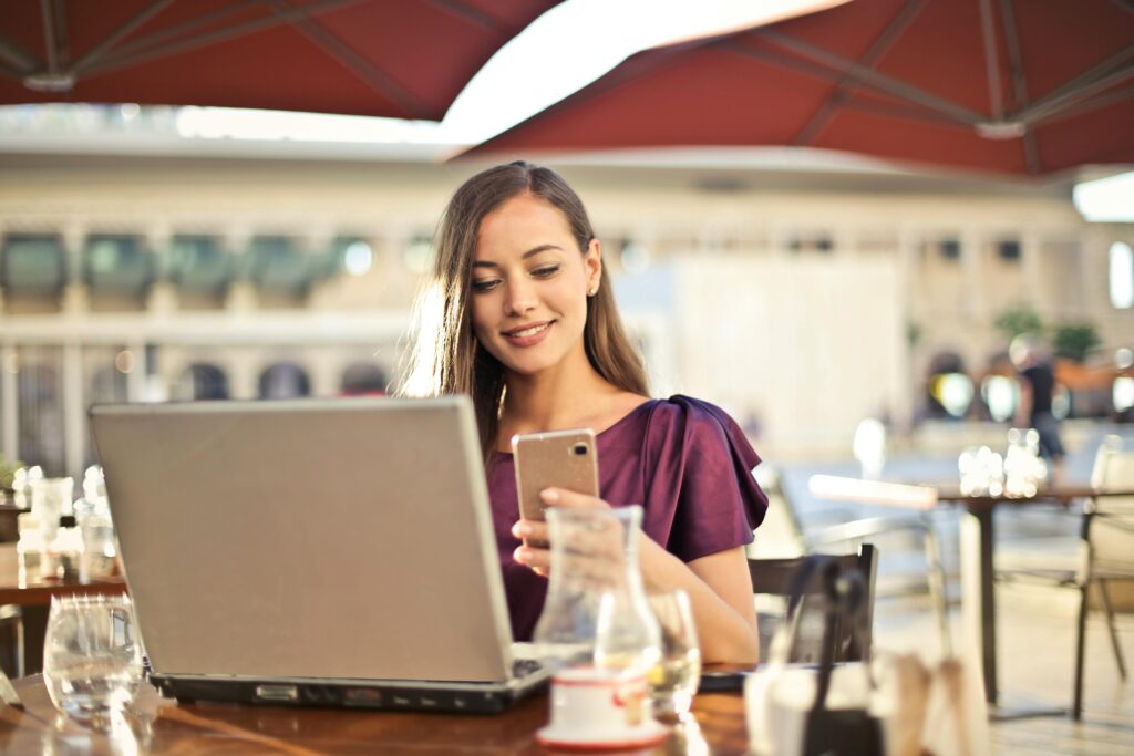 A woman real estate agent works on her laptop while enjoying a drink outside at a restaurant.
