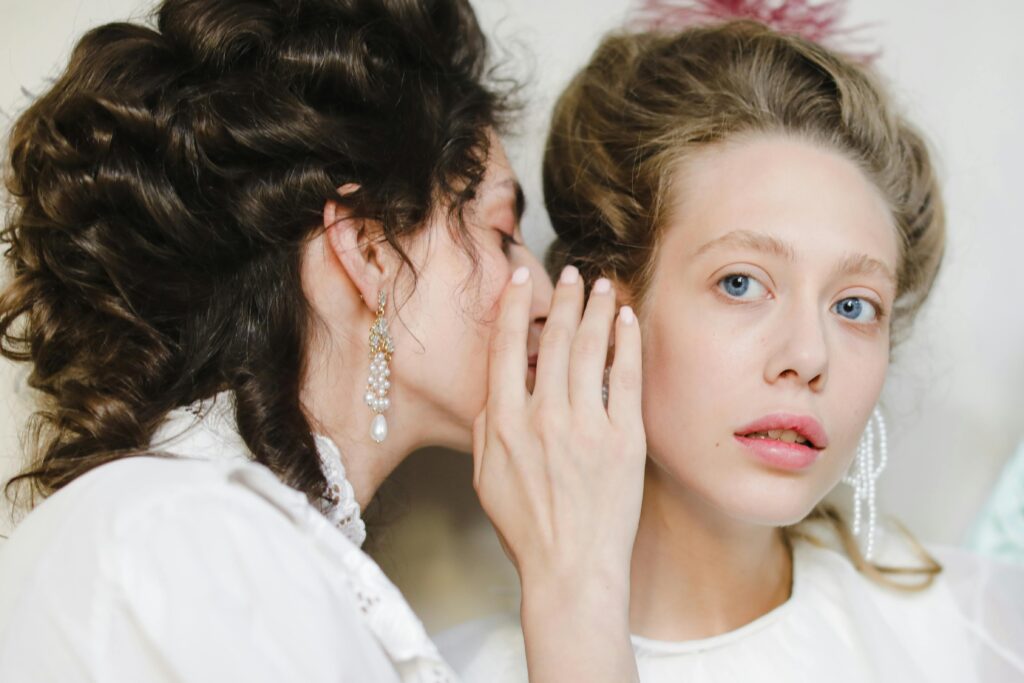 Woman whispering into the ear of another woman, perhaps referring her as a real estate client after cost-effective marketing strategies and mailers