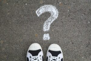 Looking down at feet towards a question mark drawn in chalk on asphalt pavement, representing your “why” in your real estate brand story.