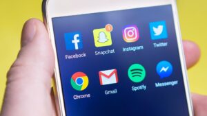 A person's hand holding a smartphone displaying social media and communication apps, representing real estate social media marketing for agents and teams