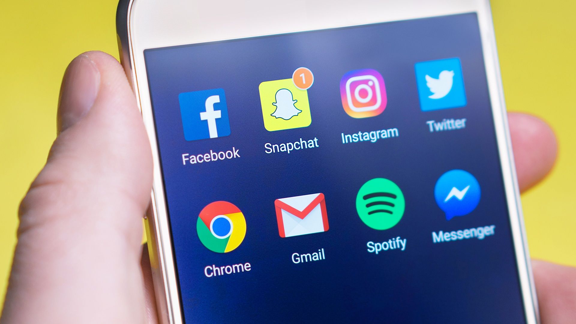 A person's hand holding a smartphone displaying social media and communication apps, representing real estate social media marketing for agents and teams